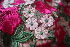 closeup of pink and green embroidered fabric with flowers on it's side, being held by someone