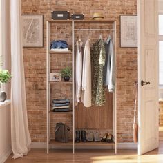 an open closet with clothes and shoes hanging on the wall next to a brick wall