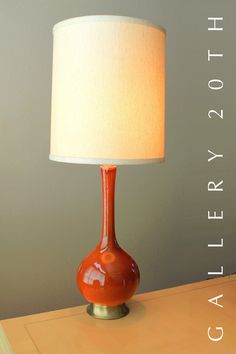 an orange lamp sitting on top of a wooden table next to a white light shade