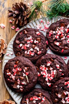 chocolate cookies with candy canes and sprinkles on a plate next to pine cones