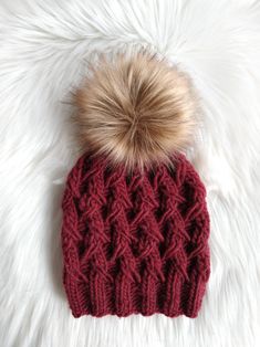 a knitted hat with a pom - pom sits on a white fur rug