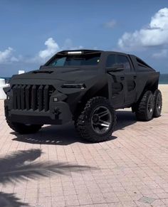 a black hummer truck parked on top of a brick road next to the ocean