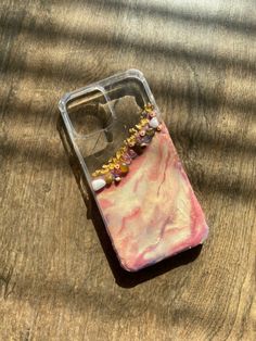 a cell phone case with beads on it sitting on top of a wooden table next to a pair of glasses