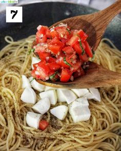 a wooden spoon with some food on top of it in a bowl next to noodles