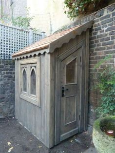 a small wooden outhouse sitting next to a brick wall and potted planter