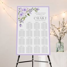 a purple and white wedding seating chart on a easel with lights in the background