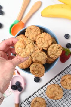 a person is holding a muffin over a bowl of blueberries and strawberries