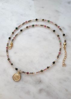 a necklace with a gold coin on it and beads hanging from the end, sitting on a marble surface