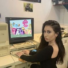 a woman sitting in front of a computer with pony ponies on the monitor screen