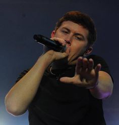 a man in black shirt holding a microphone up to his mouth while standing on stage