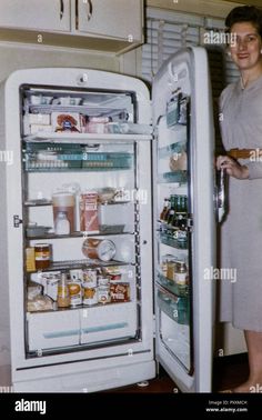 a woman standing in front of an open refrigerator full of food and drinks - stock image