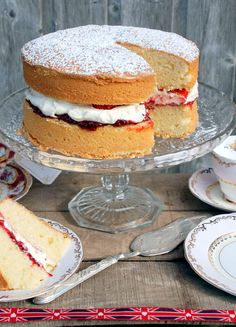 a cake sitting on top of a glass platter next to two plates and cups