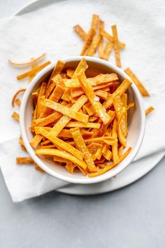 a white bowl filled with cheesy fries on top of a cloth covered table