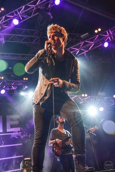 a man standing on top of a stage while holding a microphone in his hand and singing