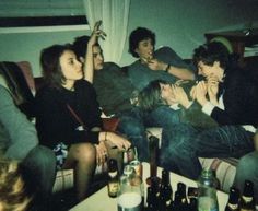 a group of people sitting around each other in a living room with bottles on the floor