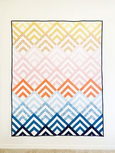 a colorful quilt hanging on the wall next to a white wall with a blue, orange and yellow pattern