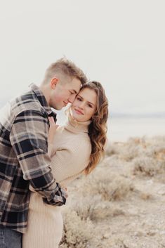 a man and woman standing next to each other in the desert with their arms around each other