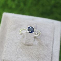 a ring with a blue stone on it sitting on a white cloth in front of some green grass