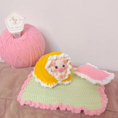 a pink ball of yarn sitting next to a crocheted baby blanket with a stuffed animal on it