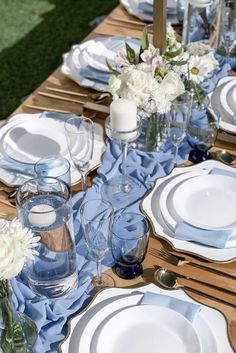 the table is set with blue and white plates, silverware, and vases