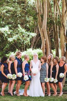 a group of women standing next to each other in front of trees and bushes with bouquets