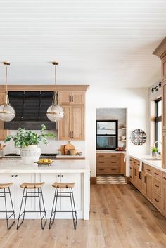 a large kitchen with wooden cabinets and white counter tops, two stools at the island