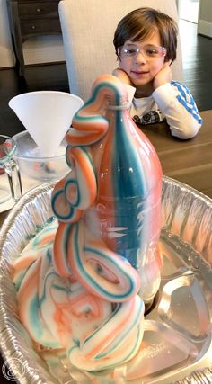 a young boy sitting at a table in front of a glass vase with swirls on it