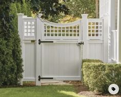 a white gate in front of a house with bushes around it and the door is open