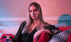 a woman sitting on top of a red couch next to a white and black pillow