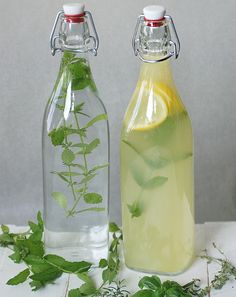 two glass bottles filled with lemonade and herbs