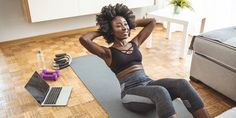 a woman sitting on a yoga mat with her laptop and exercise equipment in the background