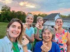 a group of women standing next to each other in front of a building at sunset