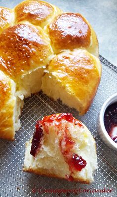 a piece of bread with jelly on it next to a bowl of jam and a roll