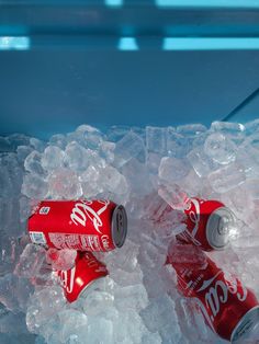 two cans of coca - cola sitting on top of ice