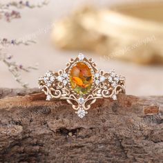 an orange and white diamond ring sitting on top of a piece of drift wood with flowers in the background