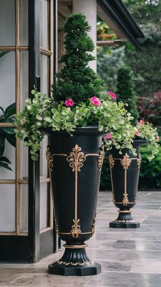 two large black vases with flowers in them on the side of a building next to another planter