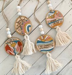 three wooden ornaments with tassels hanging from strings on a white wood background,