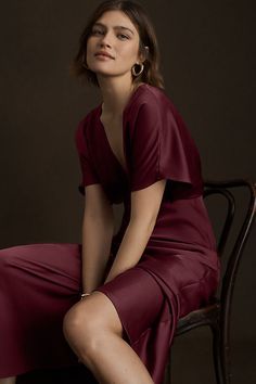 a woman in a red dress sitting on a chair with her legs crossed and looking off to the side