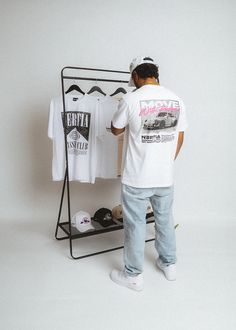 a man standing next to a rack with t - shirts hanging on it's sides