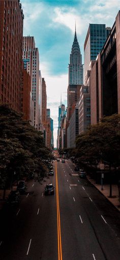 an empty city street with tall buildings on both sides and cars driving down the road