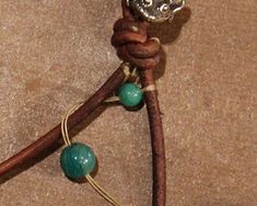 a brown leather cord with green beads and a silver metal charm on it's end