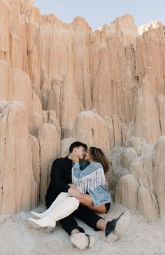 a man and woman sitting next to each other in front of rock formations with their arms around each other