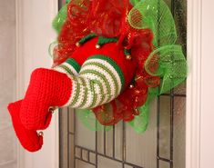 a red and green christmas wreath hanging on the front door with a knitted elf's hat