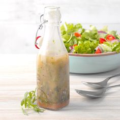 a salad in a bottle next to a bowl of salad and spoons on a table