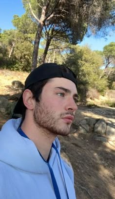 a man wearing a blue shirt and black hat standing in front of some pine trees