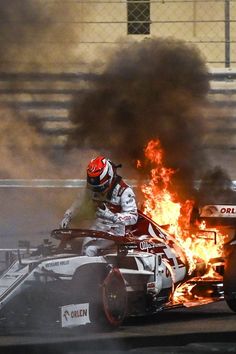 a man riding on top of a race car in front of a fire