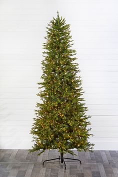 a christmas tree with lights on it in front of a white wall and wooden floor