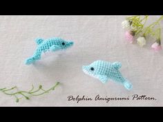 two small crocheted dolphins sitting next to each other on a table with flowers