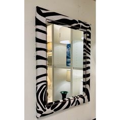 a zebra print mirror hanging on the wall next to a table lamp and two vases