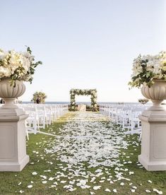 an outdoor ceremony set up with white chairs and flower petals on the ground in front of it